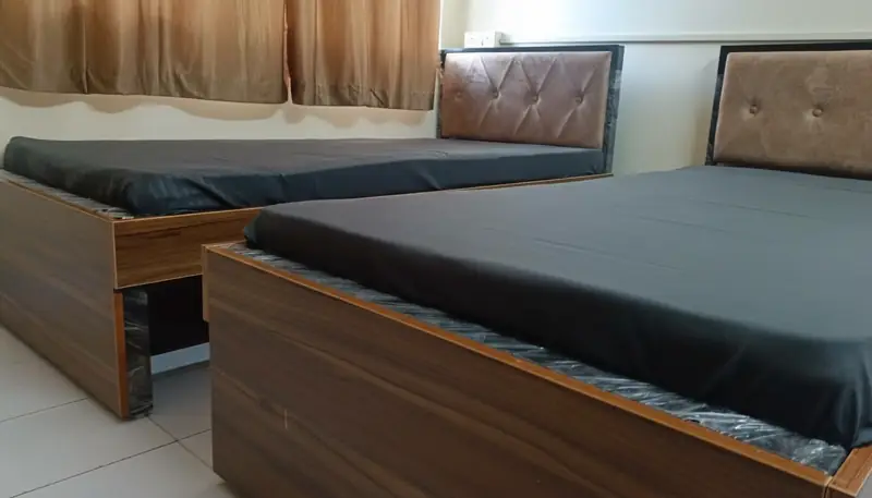 Room with two beds with padded headboards and grey bedding, curtains behind