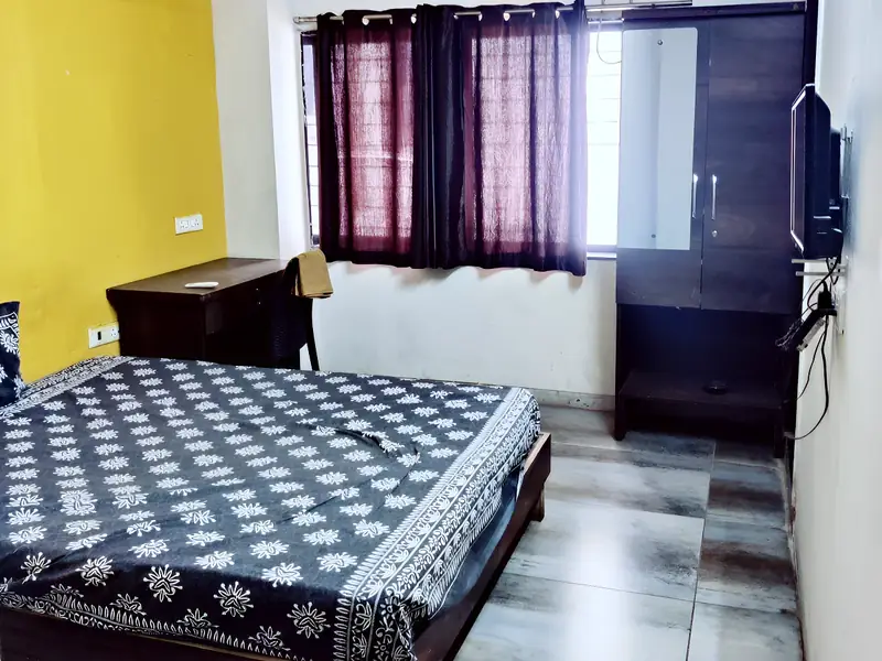 Room with a bed, ceiling fan, wall AC, TV and curtains, yellow wall